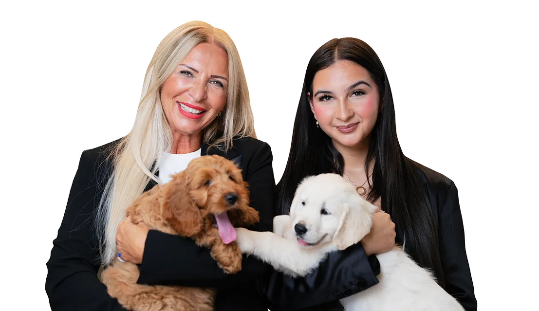 Zwei Frauen halten liebevoll einen weißen Labrador-Welpen und einen braunen Cockapoo-Welpen im Arm